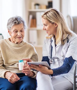 A health visitor with tablet explaining a senior woman in how to take pills. A young health visitor with tablet explaining a senior woman how to take medicine and pills.